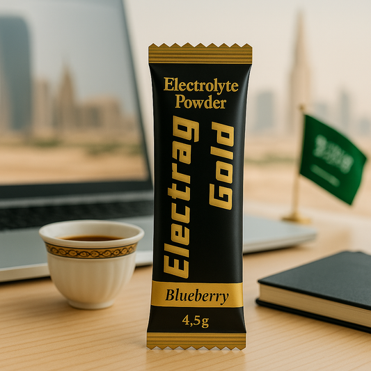 Electrag Gold sugar-free electrolyte powder sachet Blueberry 4.5g next to Arabic coffee cup, laptop, and Saudi flag — hydration for modern Saudi lifestyle