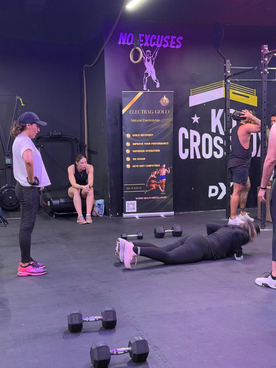 fitness trainer holding Electrag Gold sugar-free electrolyte sachet in a gym, clients exercising in the background, Dubai.