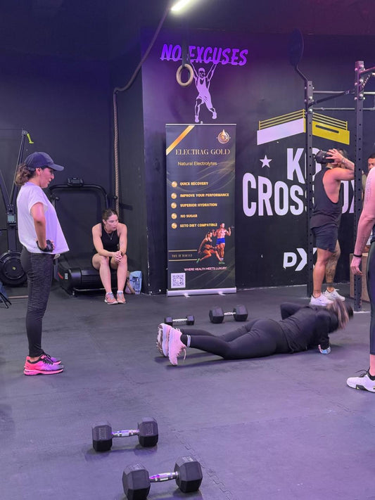 fitness trainer holding Electrag Gold sugar-free electrolyte sachet in a gym, clients exercising in the background, Dubai.